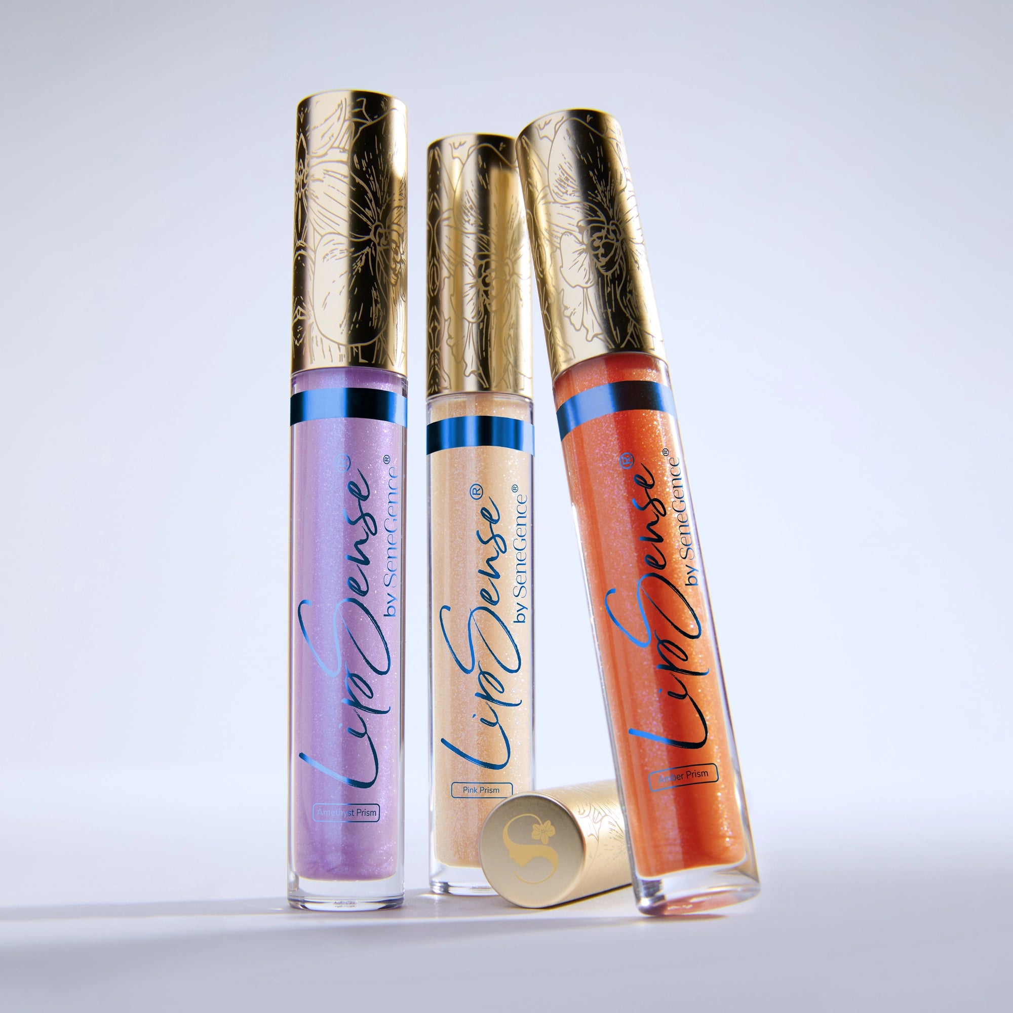 Three LipSense Prismatic gloss tubes with ornate gold caps standing upright.