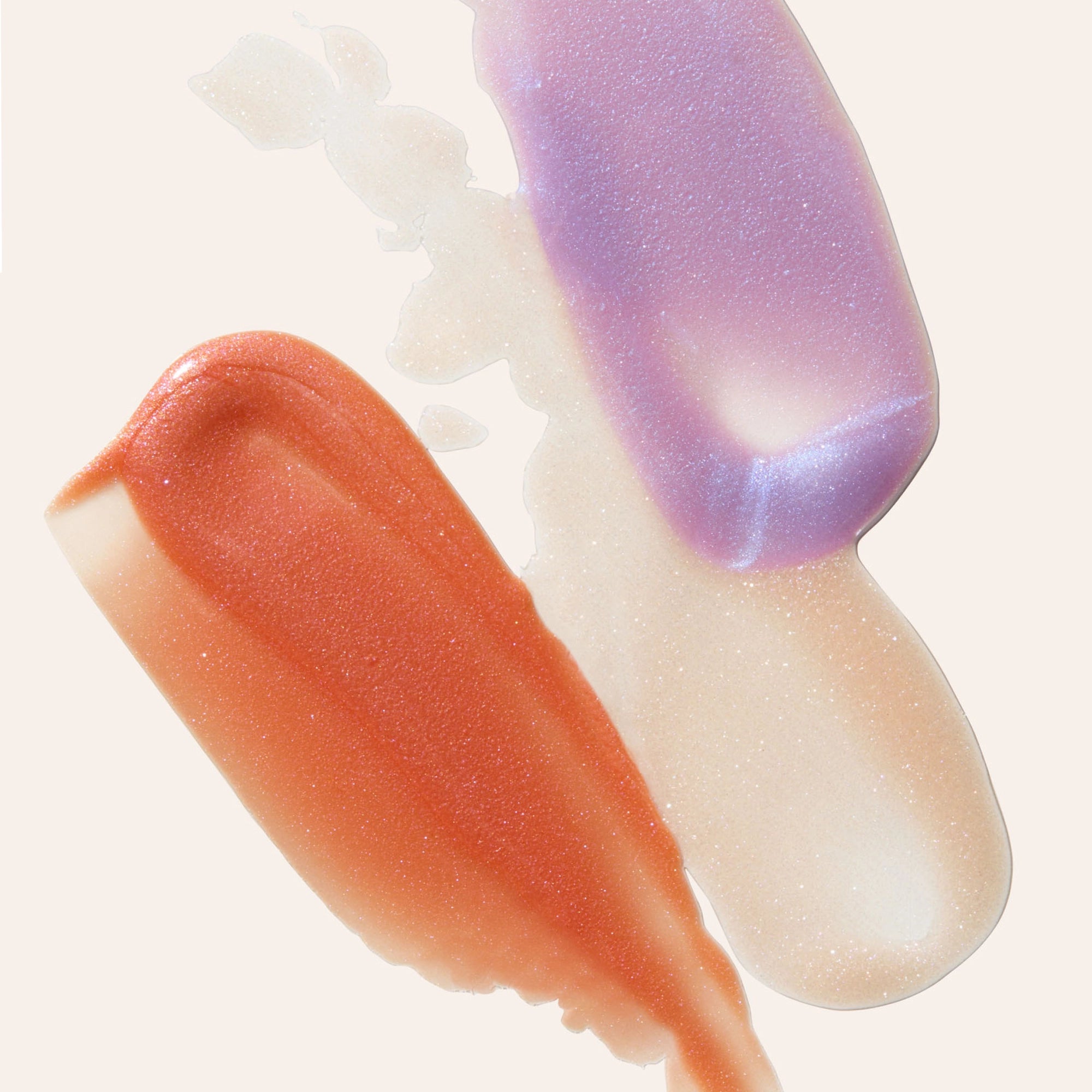 Close up of peach lavender and iridescent lip gloss swatches on a pale background